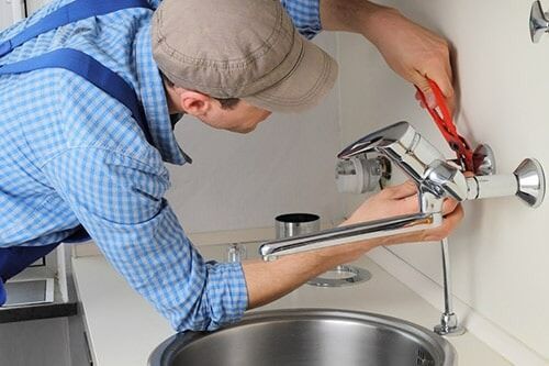Plumber Repairing Tap in a Kitchen — Plumber Repair in Armidale, NSW