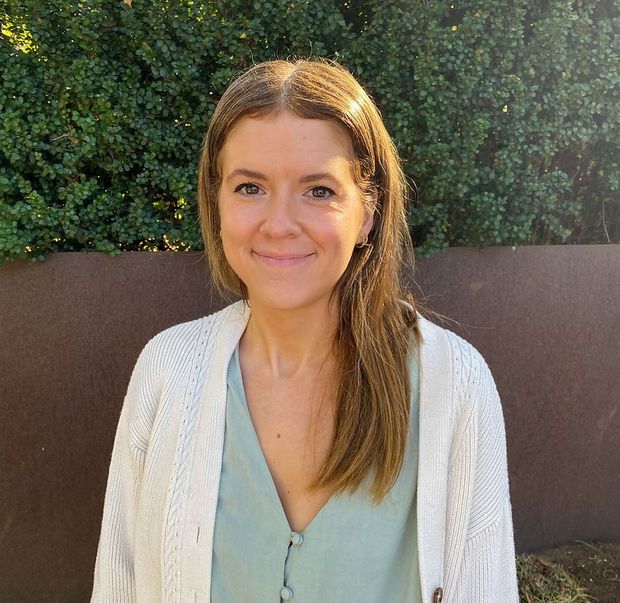 A woman wearing a white cardigan and a green shirt is smiling for the camera.