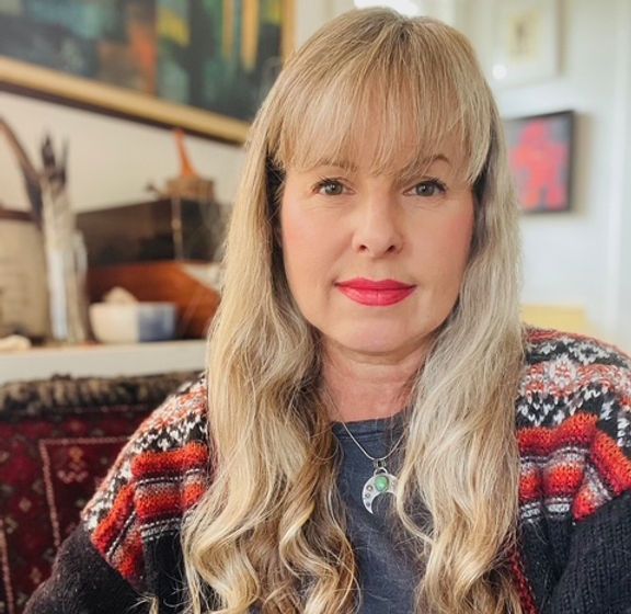 A woman with long blonde hair is wearing a sweater and a necklace.