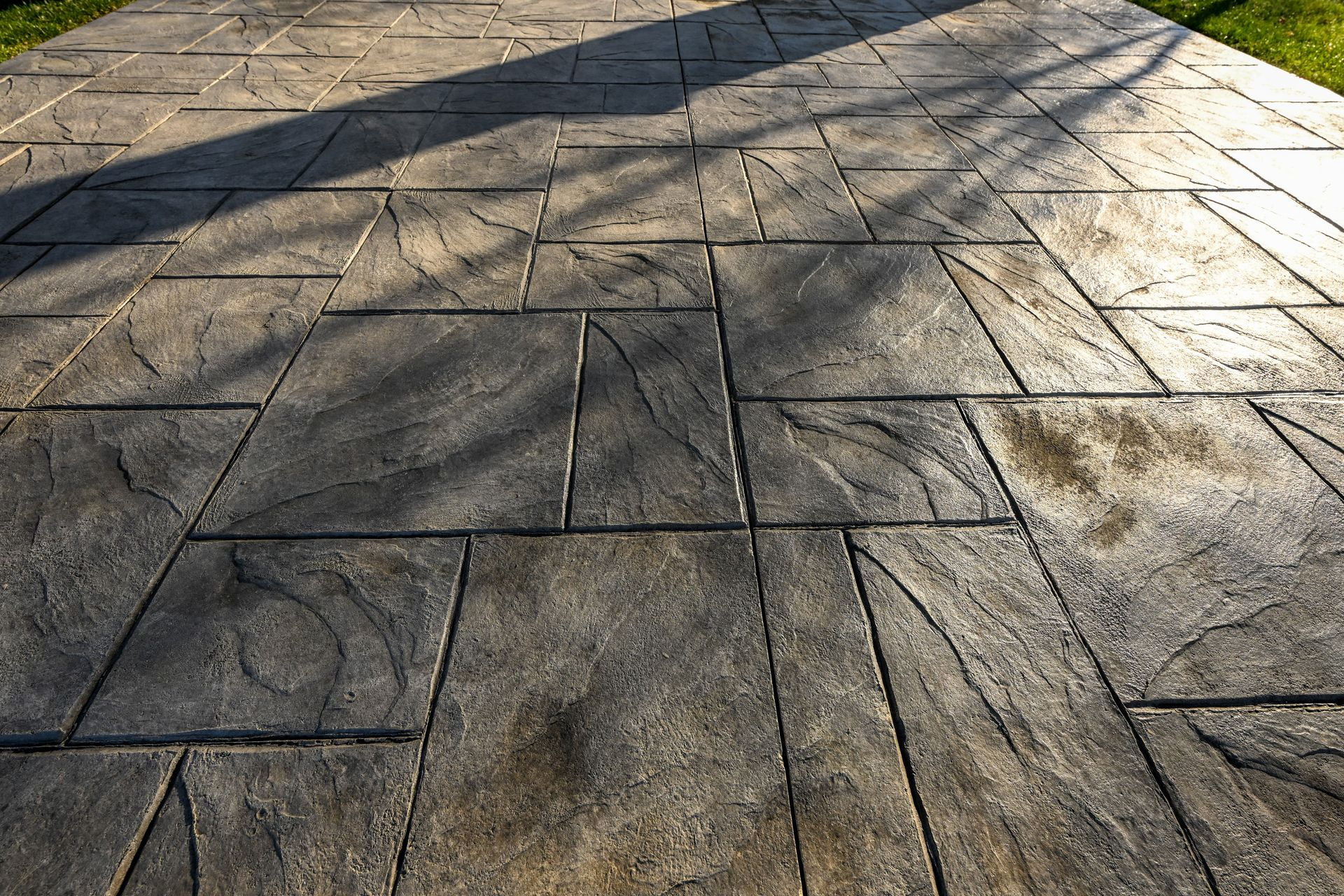 Close-up view of stamped concrete surface with slate-like texture and dark stain, showing natural li