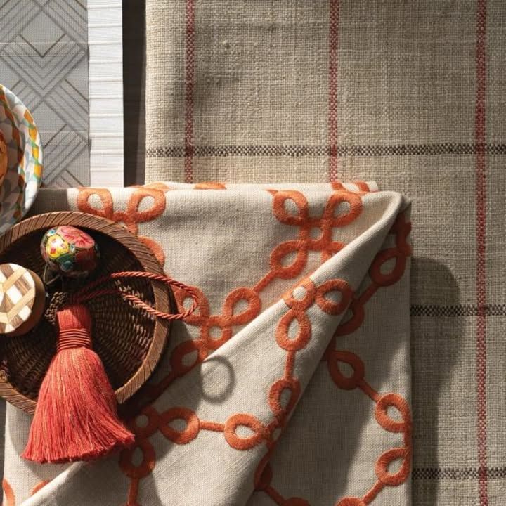 A folded beige napkin with orange chain design, near a woven tray with tassel, and striped fabric.