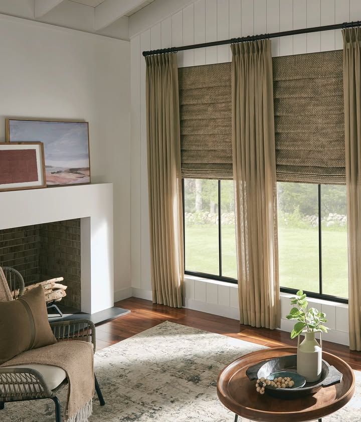 Living room with fireplace, windows, and neutral-toned curtains and blinds.