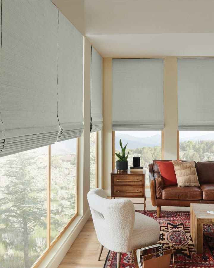 Living room with light-colored Roman shades, brown leather sofa, and a fuzzy white chair.