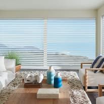 Living room with ocean view through striped blinds, couch, and coffee table with decor.