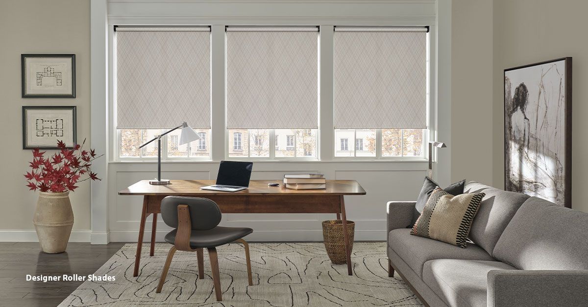 Home office with desk, window blinds, and sofa. Beige and neutral tones.