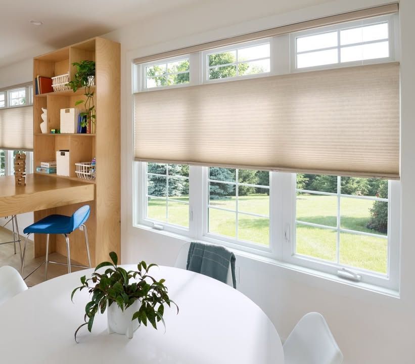 A bright dining area with tan honeycomb shades, a round table, and a kitchen bar.