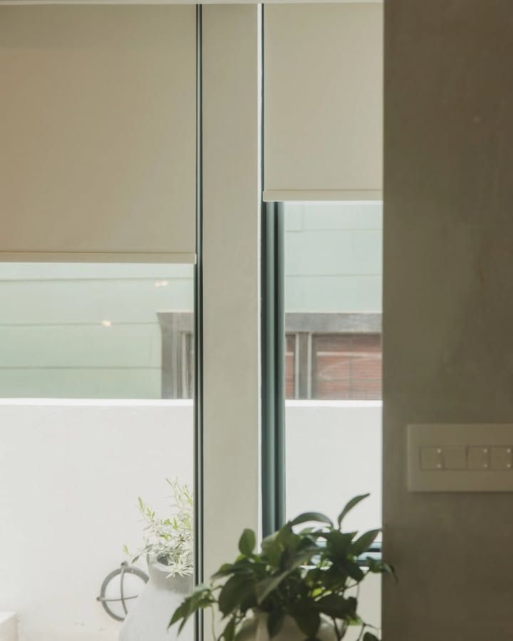 Beige roller blinds partially cover a window, revealing a glimpse of an outdoor patio and greenery.