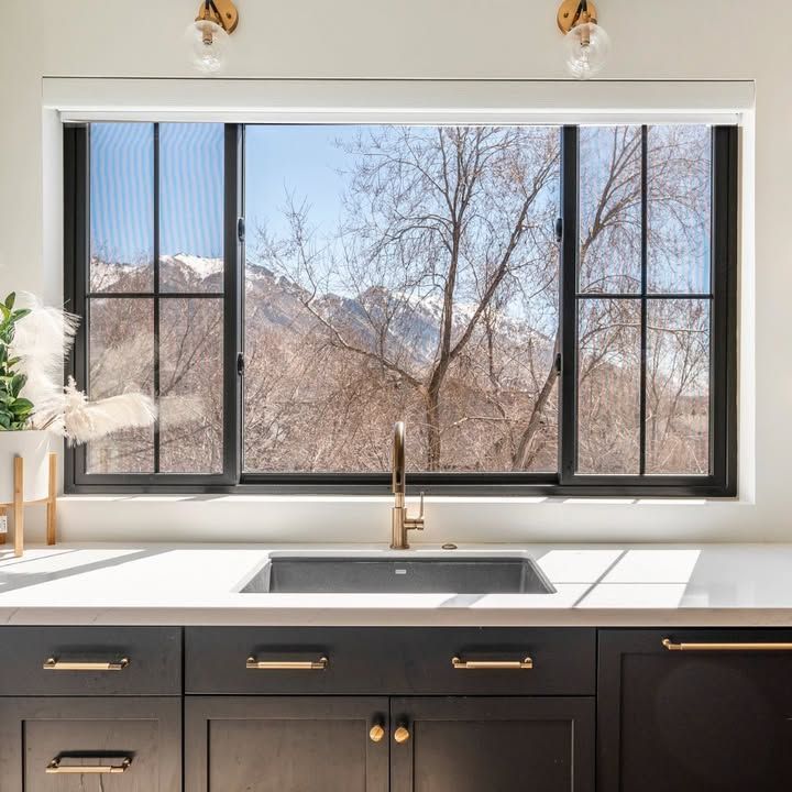 Kitchen with black cabinets, white countertop, and window overlooking mountains.