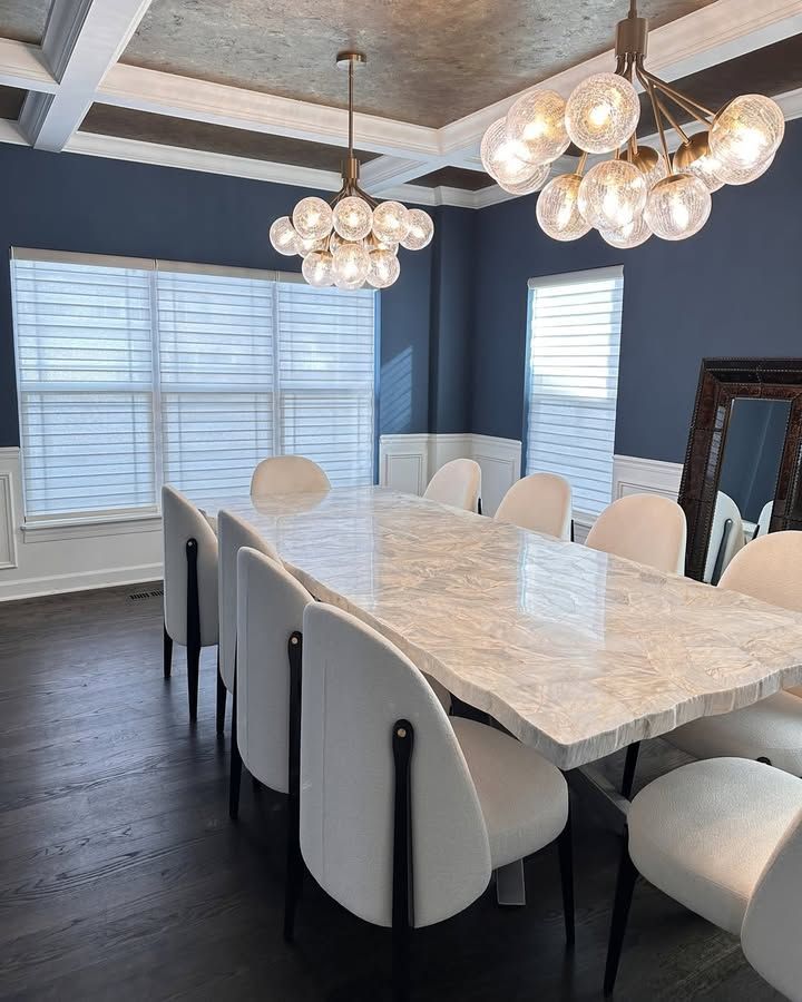 Formal dining room with large marble table, white chairs, blue walls, and two globe-light chandeliers.