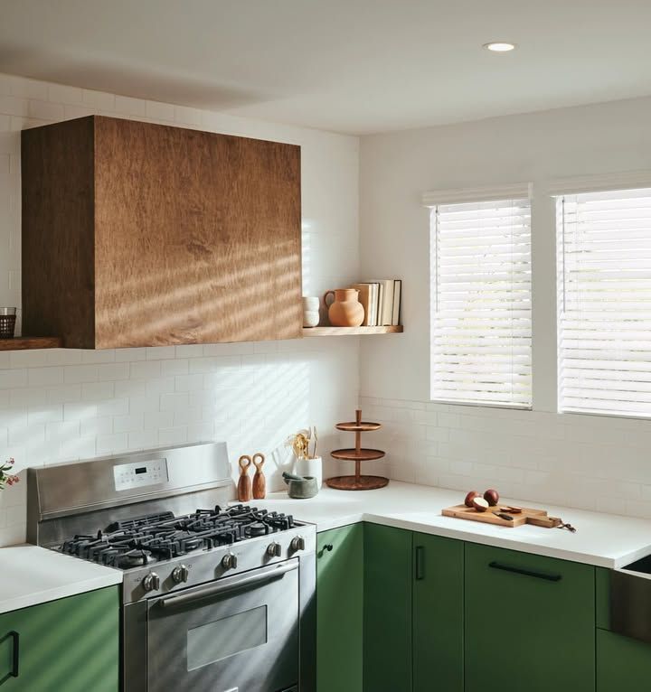 Kitchen with stainless steel stove, green cabinets, white countertops, and wooden hood.