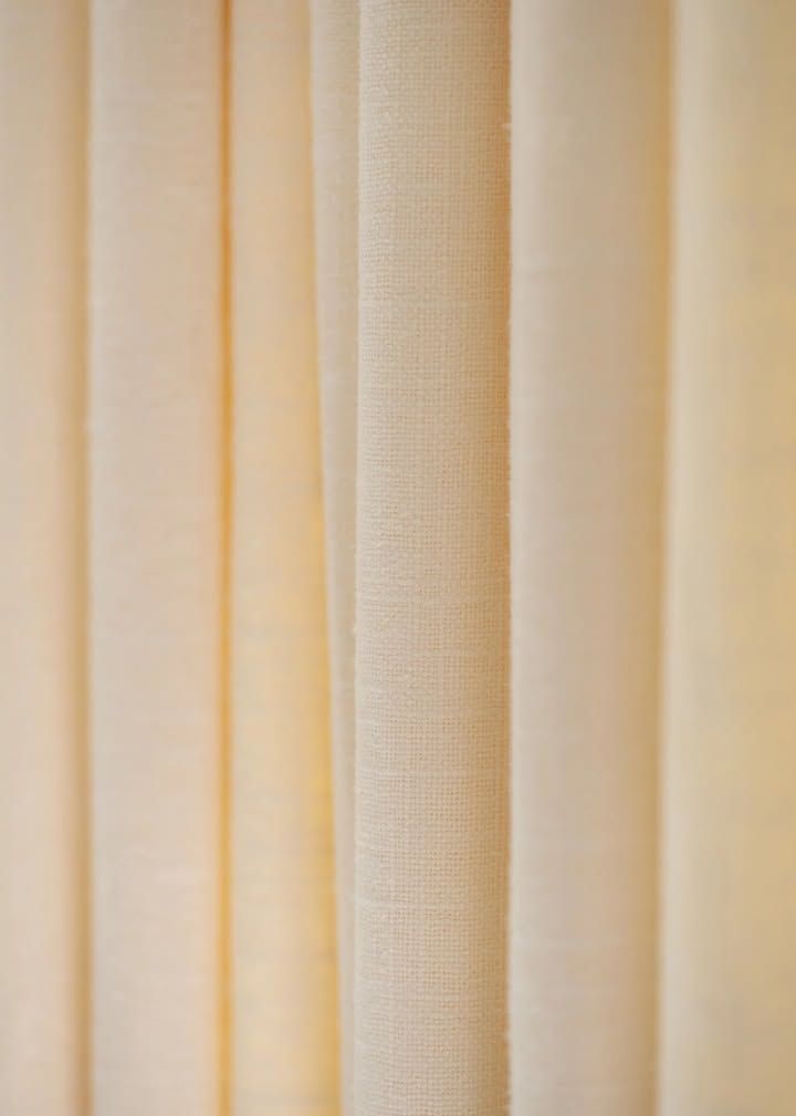 Cream-colored curtains hanging vertically, with visible folds and a textured weave.