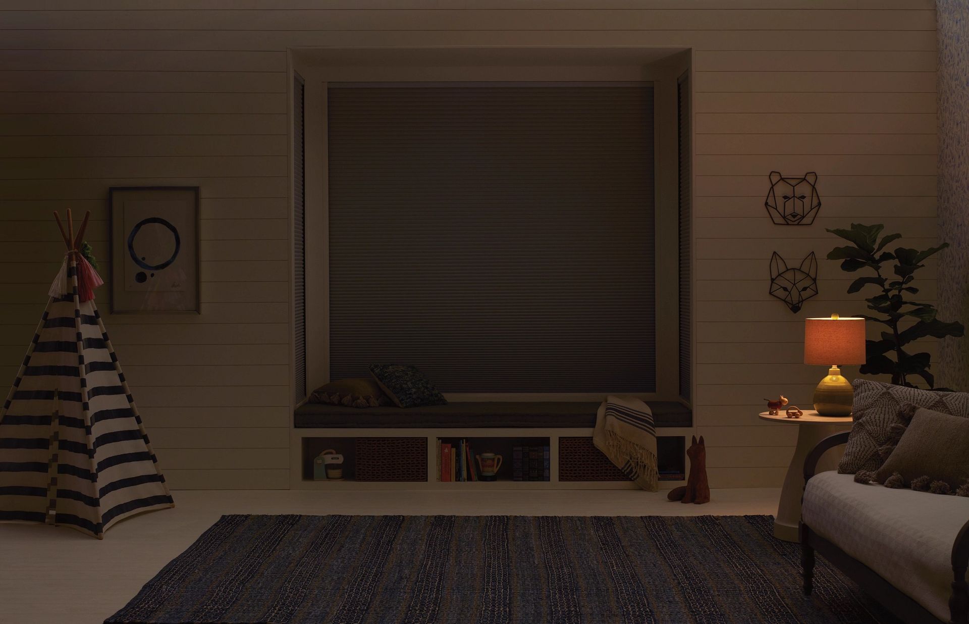 Cozy room with teepee, window seat, and rug, lit by a lamp. The window is covered with a blind.