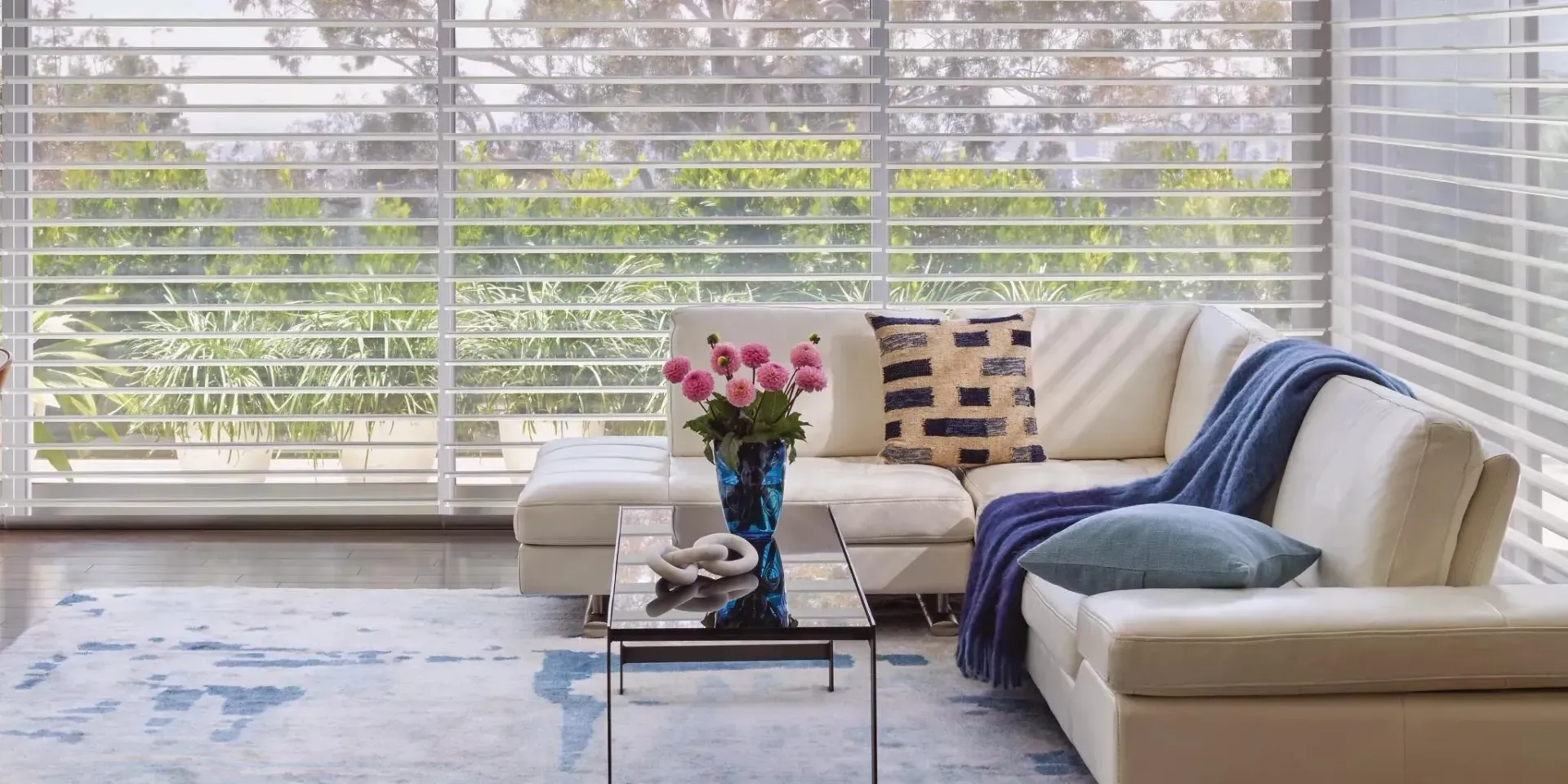 Living room with white sectional, blue rug, and large windows with a view.