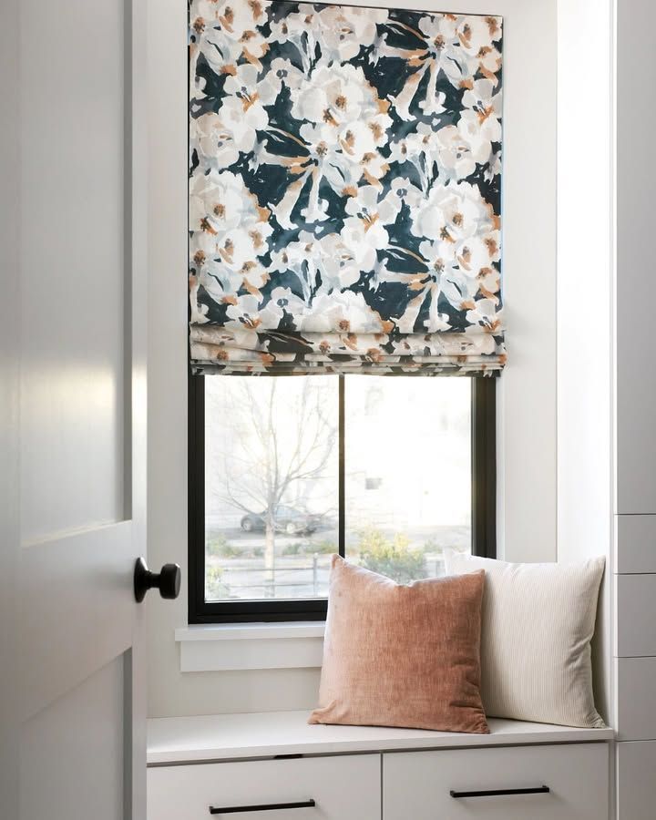 Window seat with floral Roman shade, two pillows, and a view of trees.
