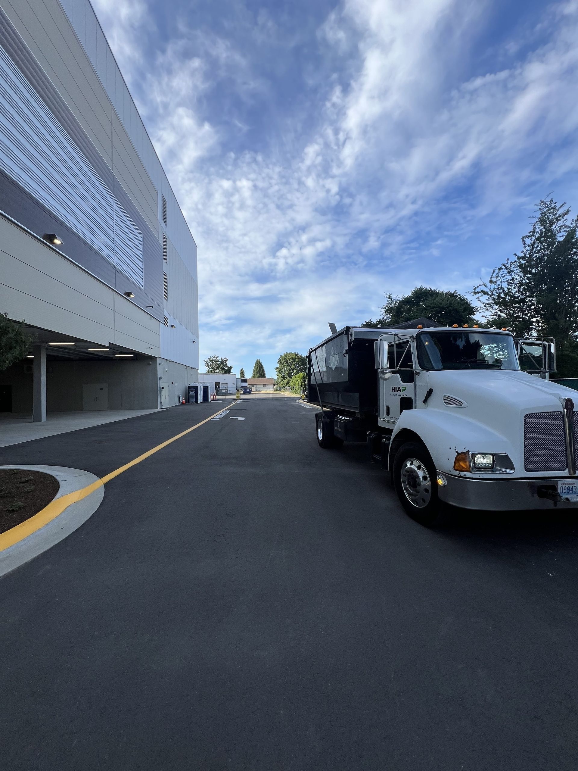 White dump truck parked on asphalt next to a modern building; cloudy sky.