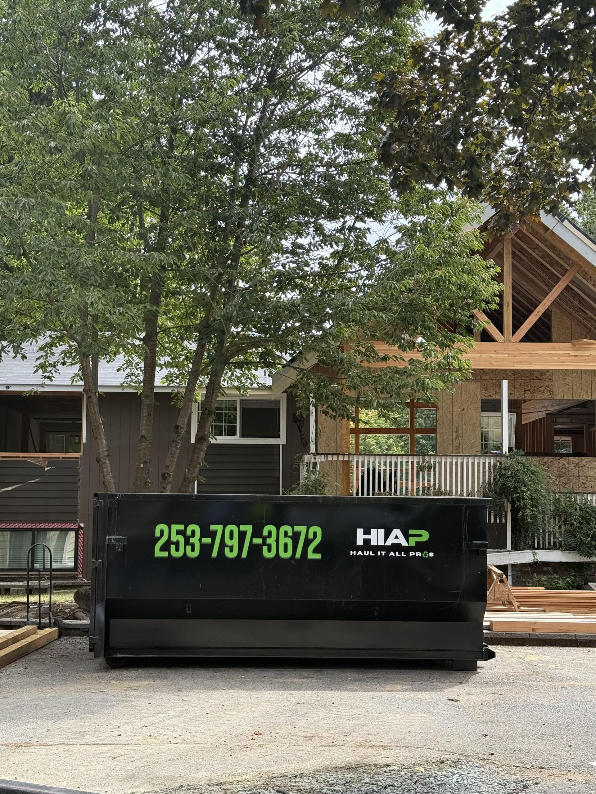 Black dumpster with phone number 253-797-3672 in front of a house under construction.