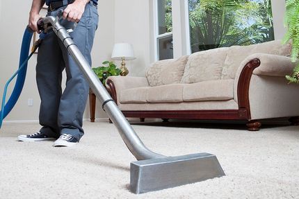A man is using a vacuum cleaner to clean a carpet in a living room.