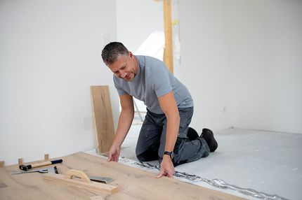 A man is kneeling on the floor while installing a wooden floor.