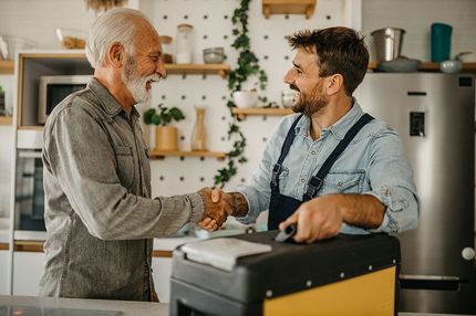 A man is shaking hands with a plumber in a kitchen.