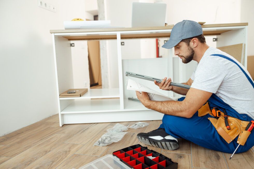 A man is kneeling on the floor working on a cabinet.