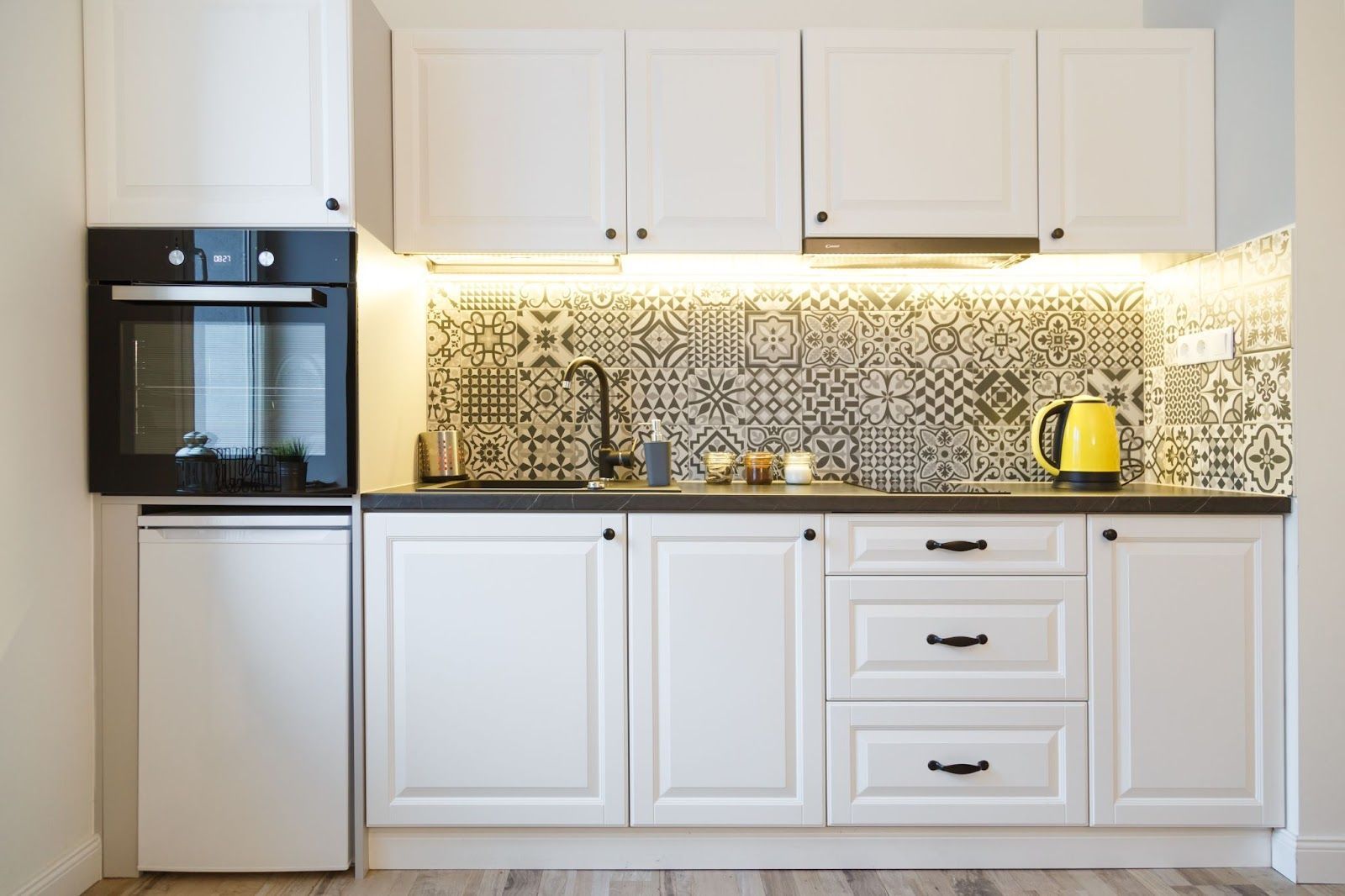 A kitchen with white cabinets , black appliances and a yellow kettle.