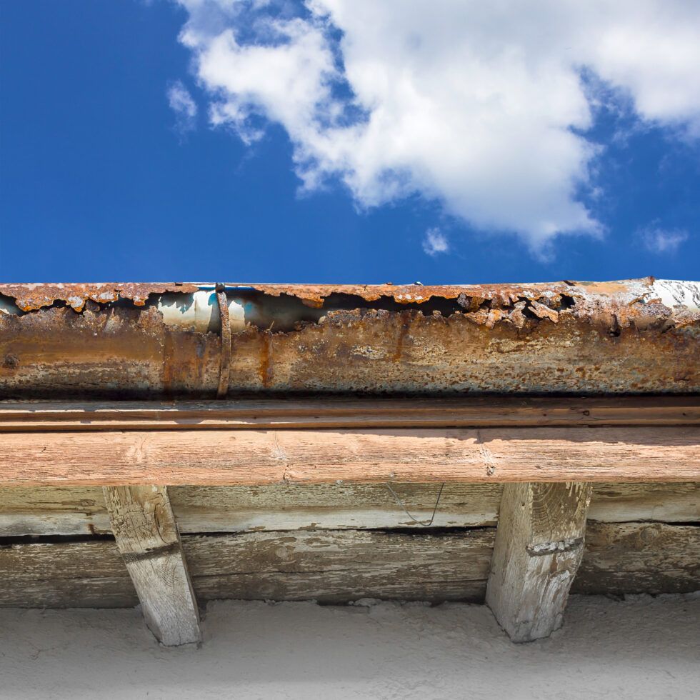 A rusty gutter on a roof with a blue sky in the background.