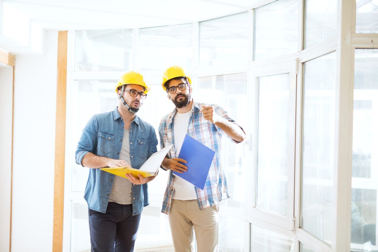 Two men in hard hats are standing next to each other in a room.