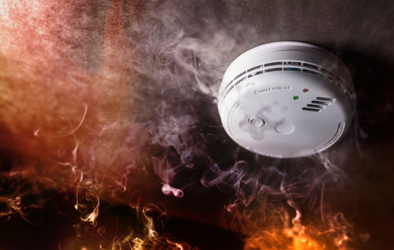 A smoke detector is surrounded by smoke and flames in a room.