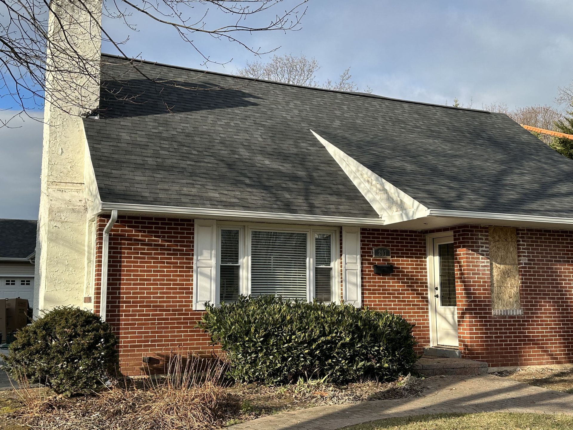 A Red brick house with white shutters, a bay window, and a white chimney