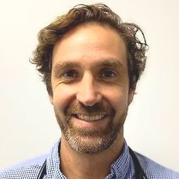A man with a beard and a stethoscope around his neck is smiling for the camera.