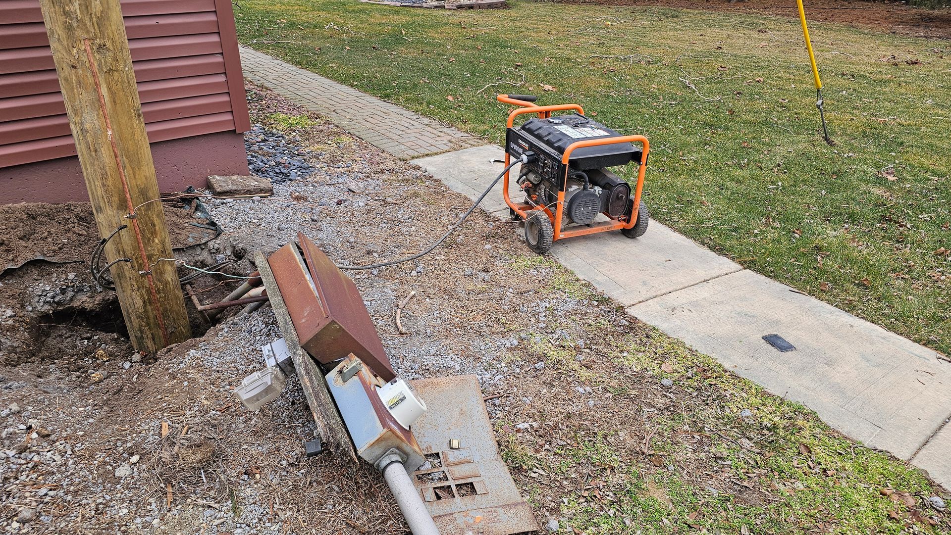 A generator is sitting on the sidewalk next to a brick wall.