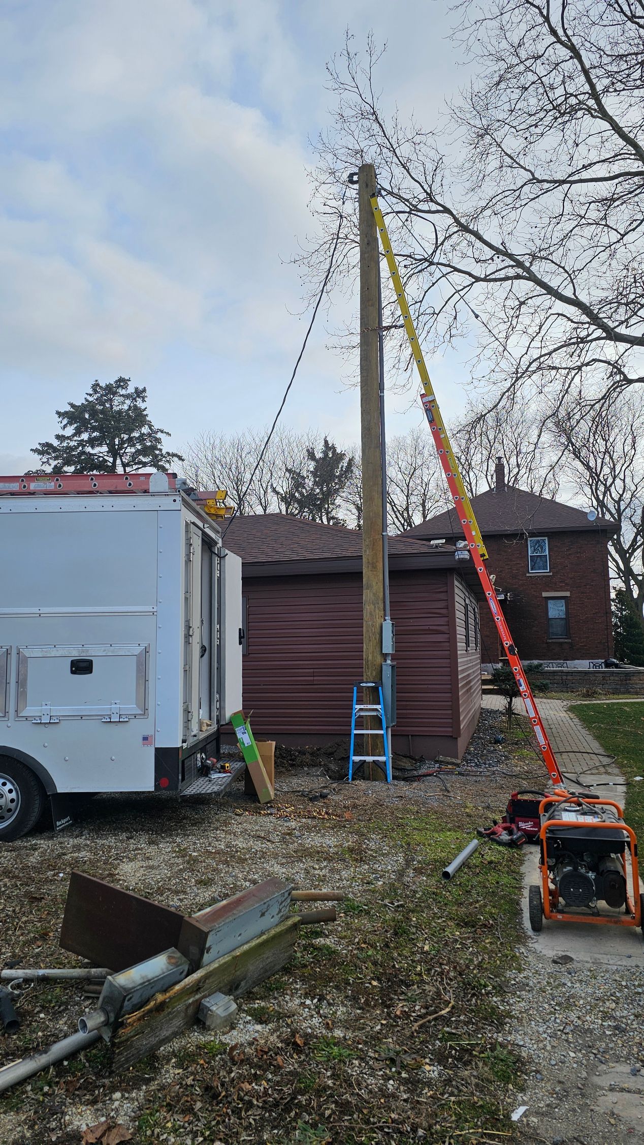 A ladder is attached to a power pole in front of a house.