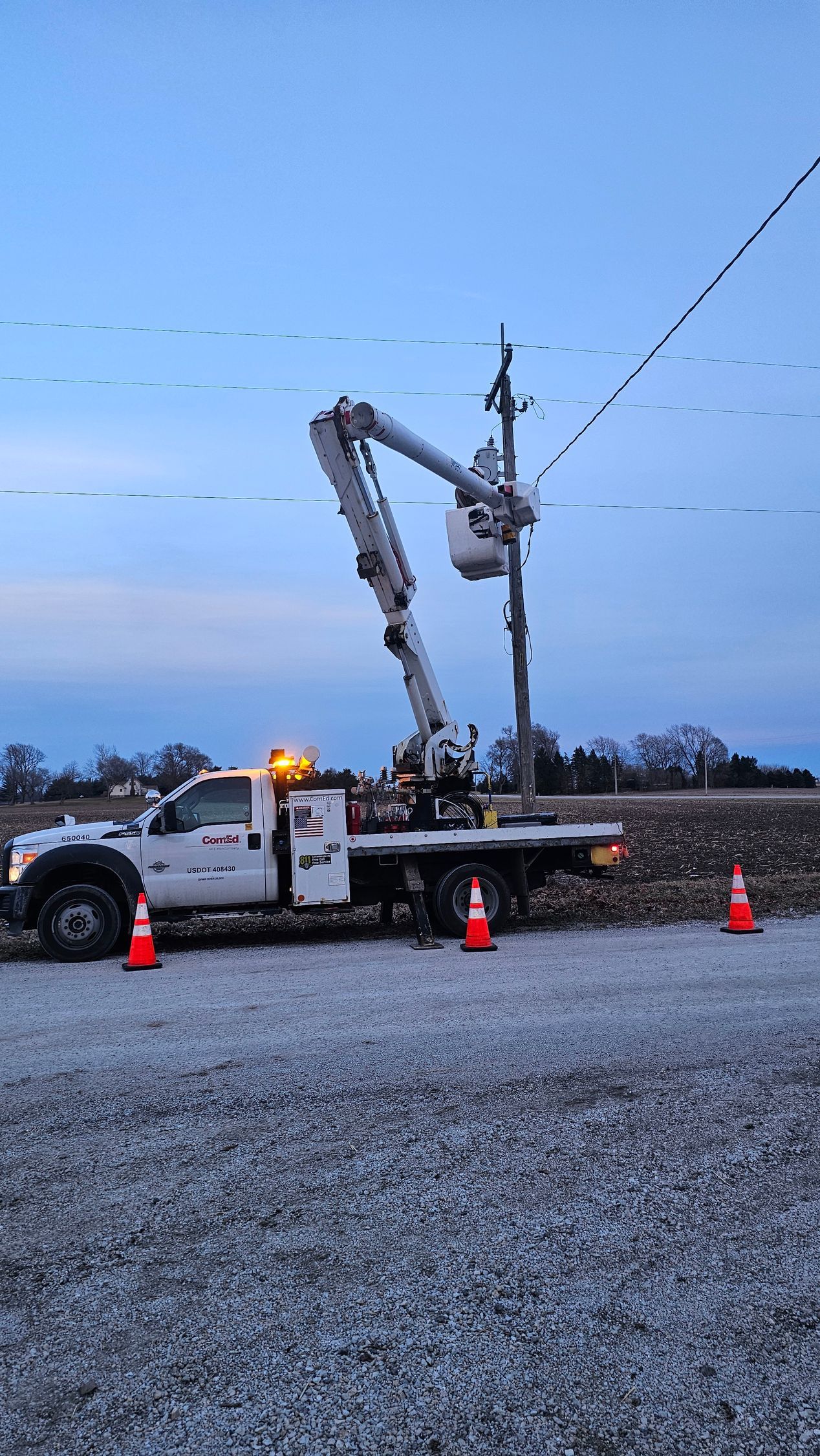 A white truck is parked in a gravel lot next to a power line.