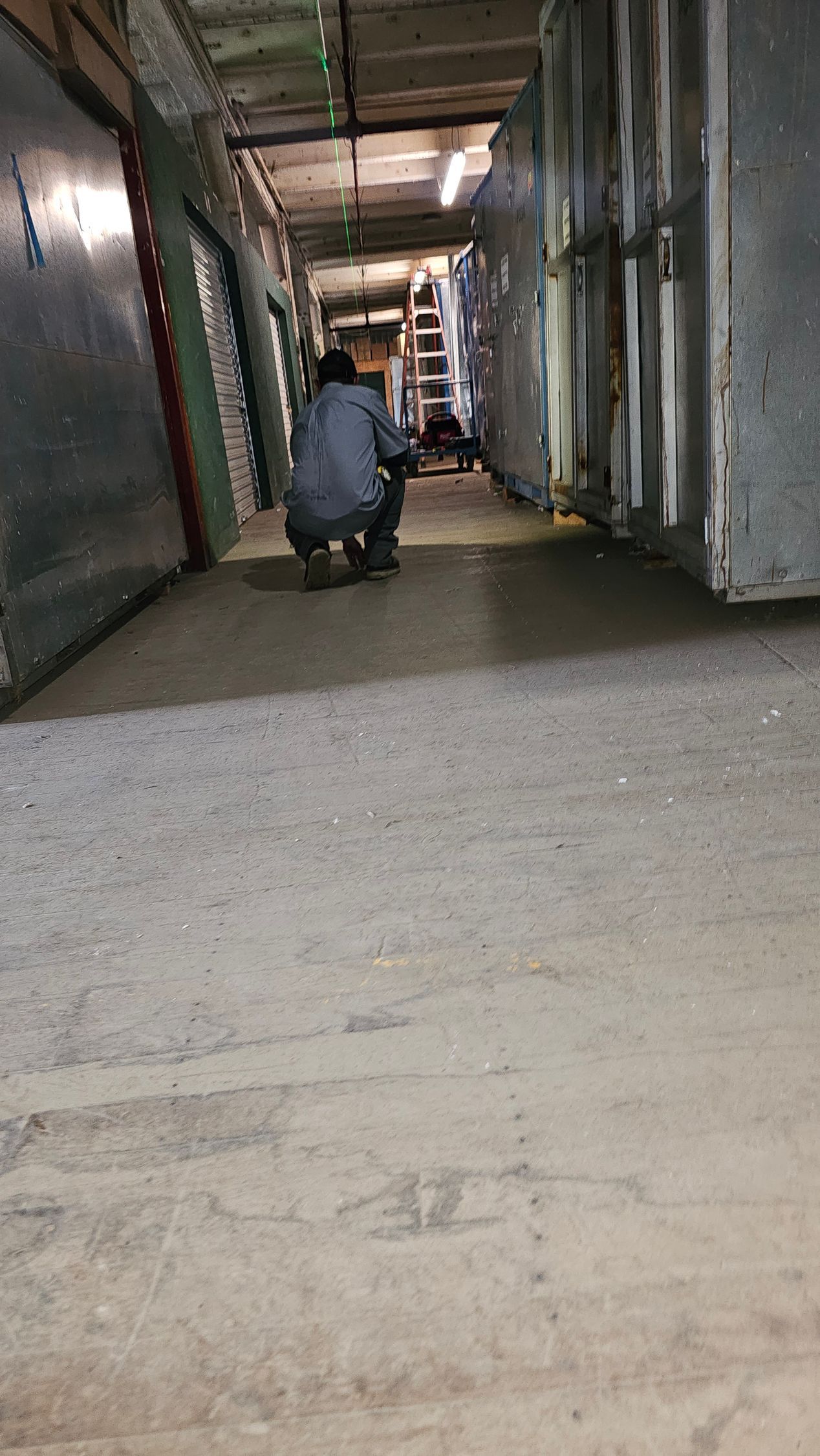 A man is squatting on the floor in a hallway.