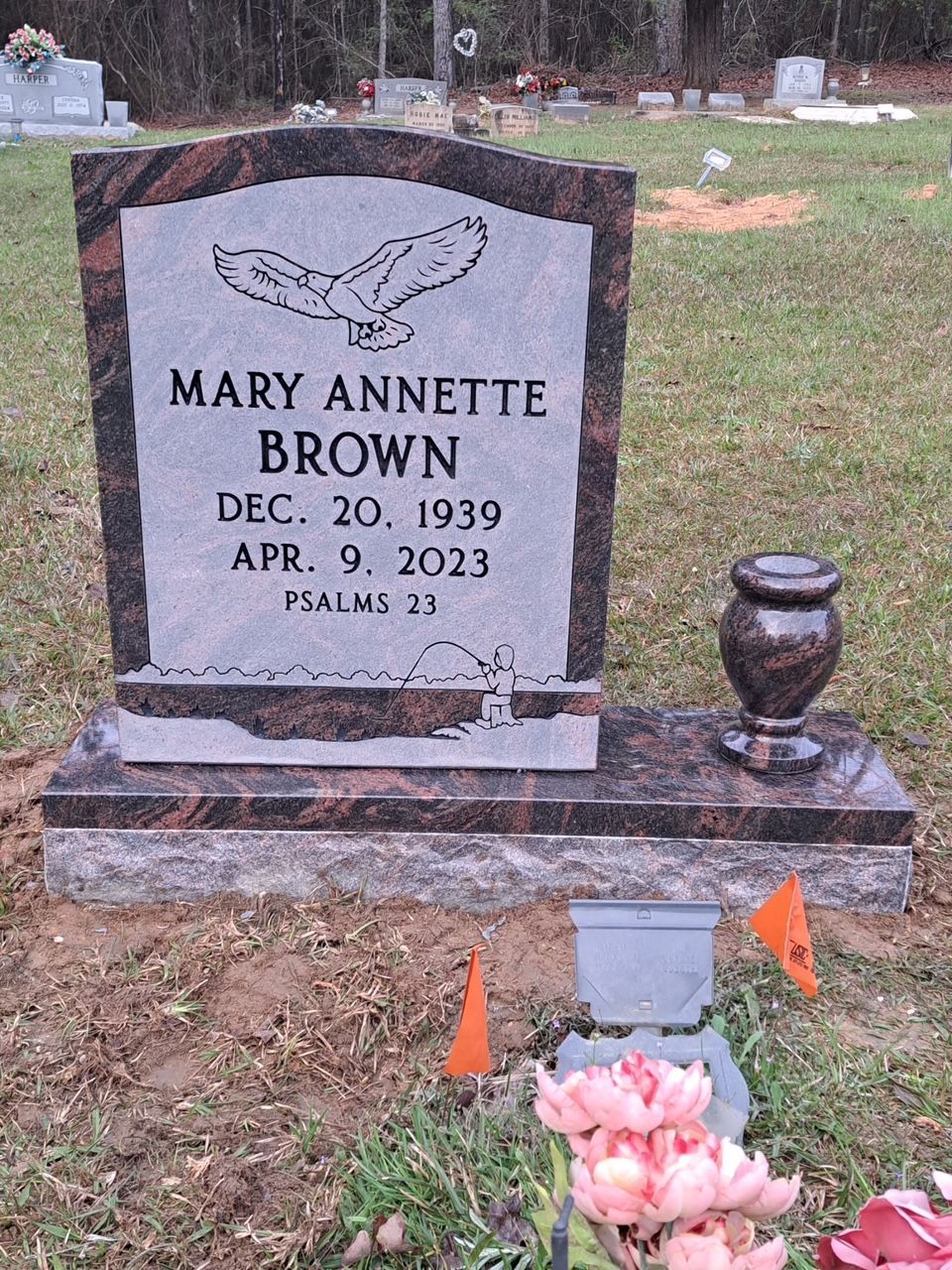 A grave marker for Mary Annette Brown, displaying an eagle engraving, dates 1939-2023, and Psalms 23 in a cemetery.