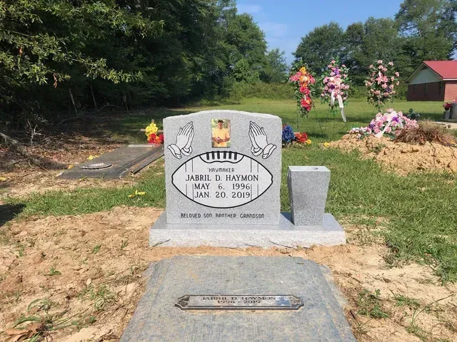 A Gravestone in a Cemetery with Flowers in the Background – Canton, MS – Davidson Marble & Granite
