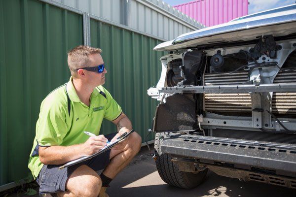 A Man in Green Shirt Inspects the Front of a Damaged Car, Taking Notes on a Clipboard — Mid City Smash Repairs in Dubbo, NSW