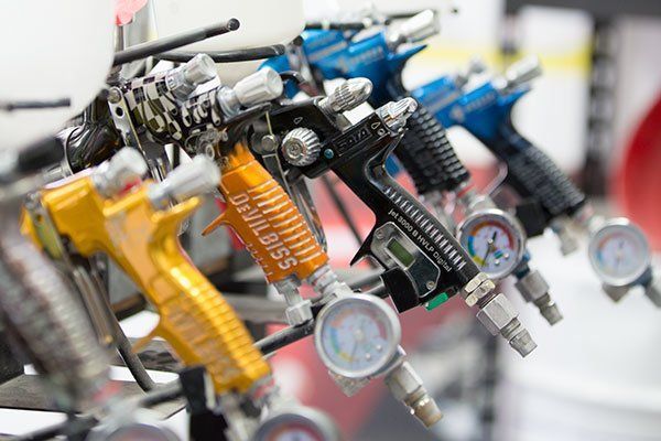 Row of Colourful Spray Paint Guns Hanging on Display — Mid City Smash Repairs in Dubbo, NSW