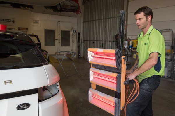 Man in Shop Using Infrared Paint Drying Lamps on White Car — Mid City Smash Repairs in Dubbo, NSW
