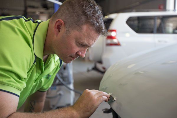 Man in Green Shirt Inspecting White Car for Damage in a Garage — Mid City Smash Repairs in Dubbo, NSW