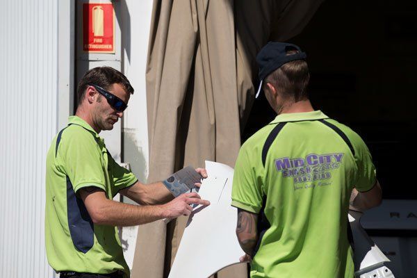 Two Men in Green Shirts Inspecting a White Object Outdoors — Mid City Smash Repairs in Dubbo, NSW