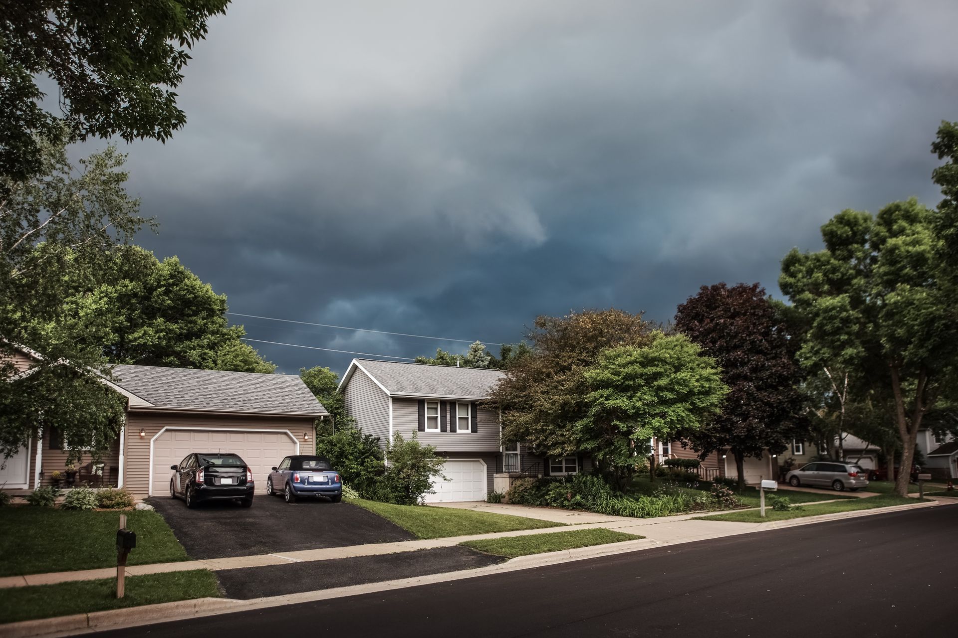Suburban homes under a dark, stormy sky; cars parked in driveways, trees lining the street.