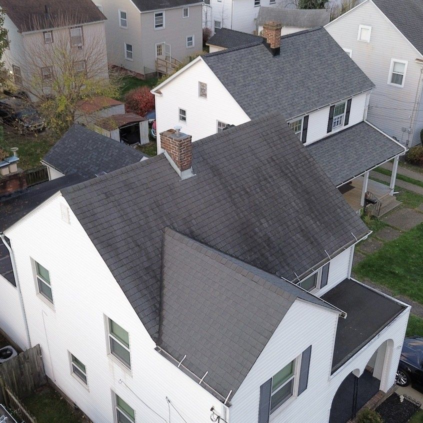 Overhead view of several white houses with dark gray roofs, surrounded by trees and other buildings.