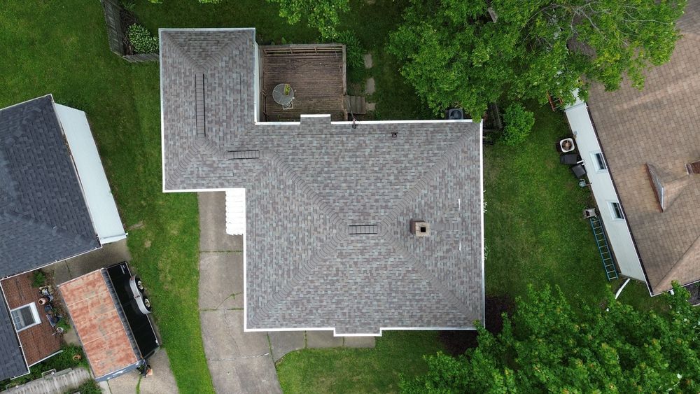 Overhead view of a gray-roofed house with a deck, surrounded by green trees and grass.