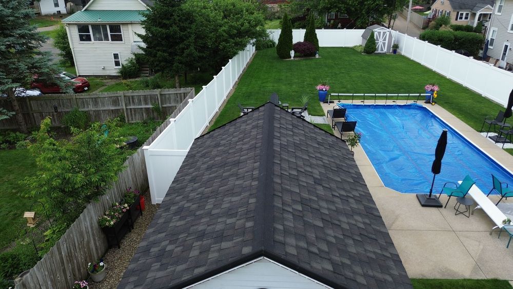 Overhead view of a house with a pool and fenced backyard. Gray shingle roof in the foreground.