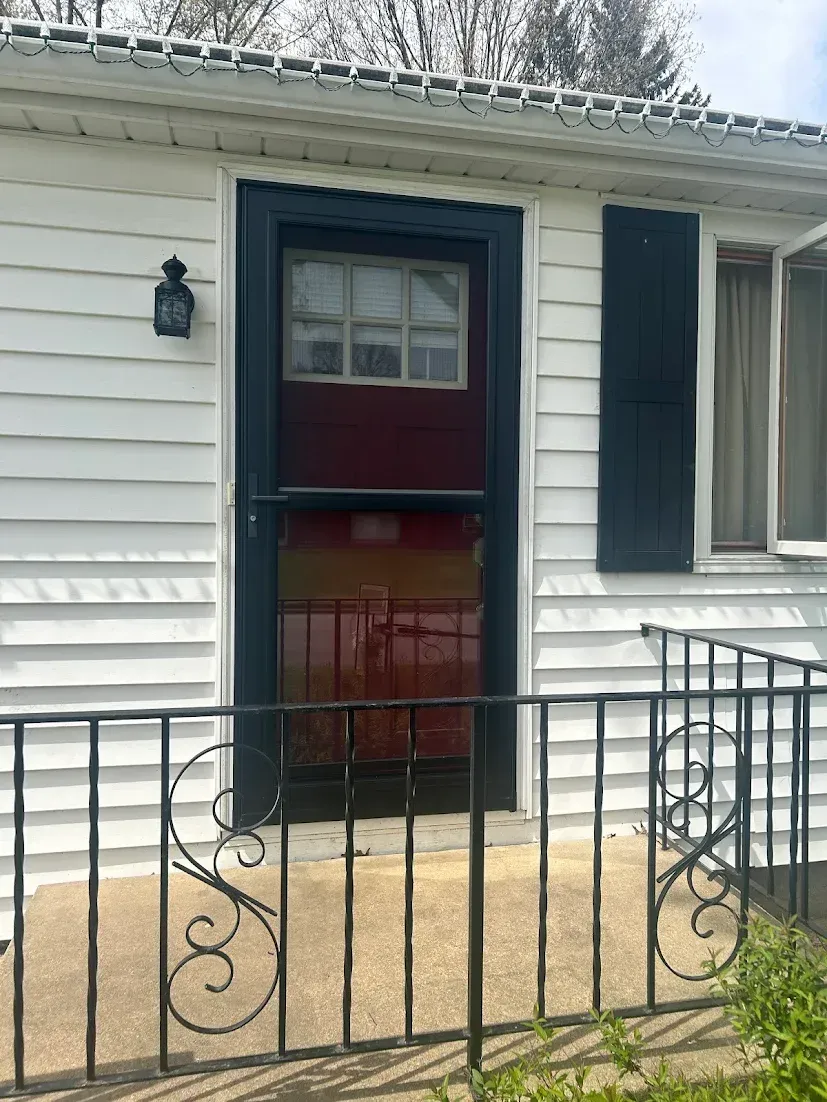 White house with black door trim and storm door; wrought iron railing.