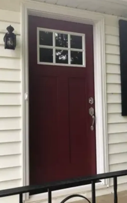 Burgundy front door with a window panel, white trim, and a black porch light.