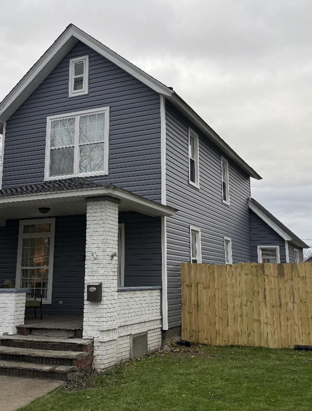 Two-story house with blue siding, white trim, and a wooden fence on a cloudy day.