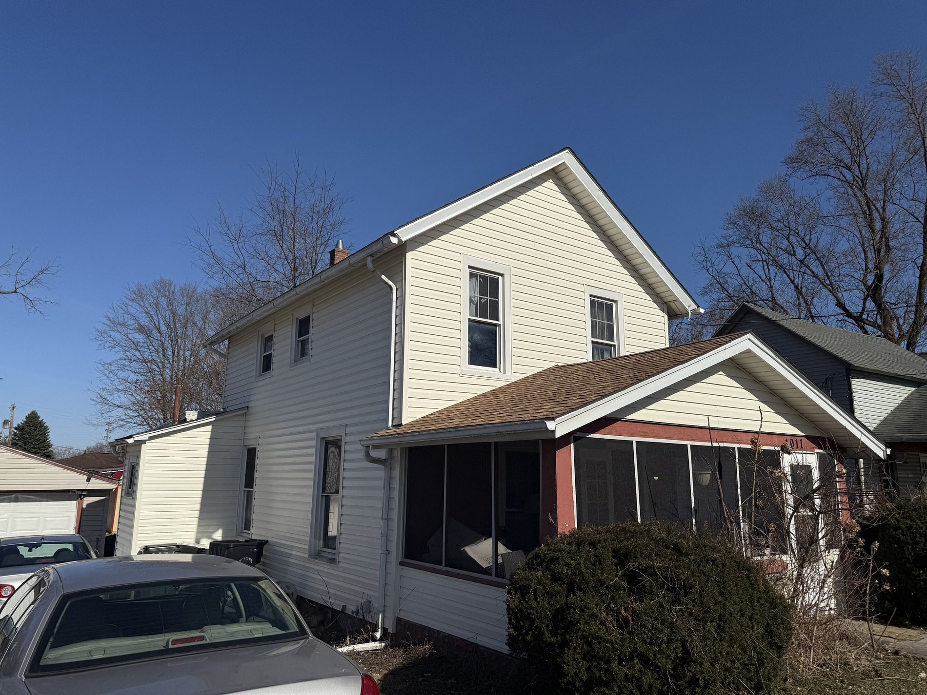 Two-story white house with a screened porch and parked cars on a sunny day.