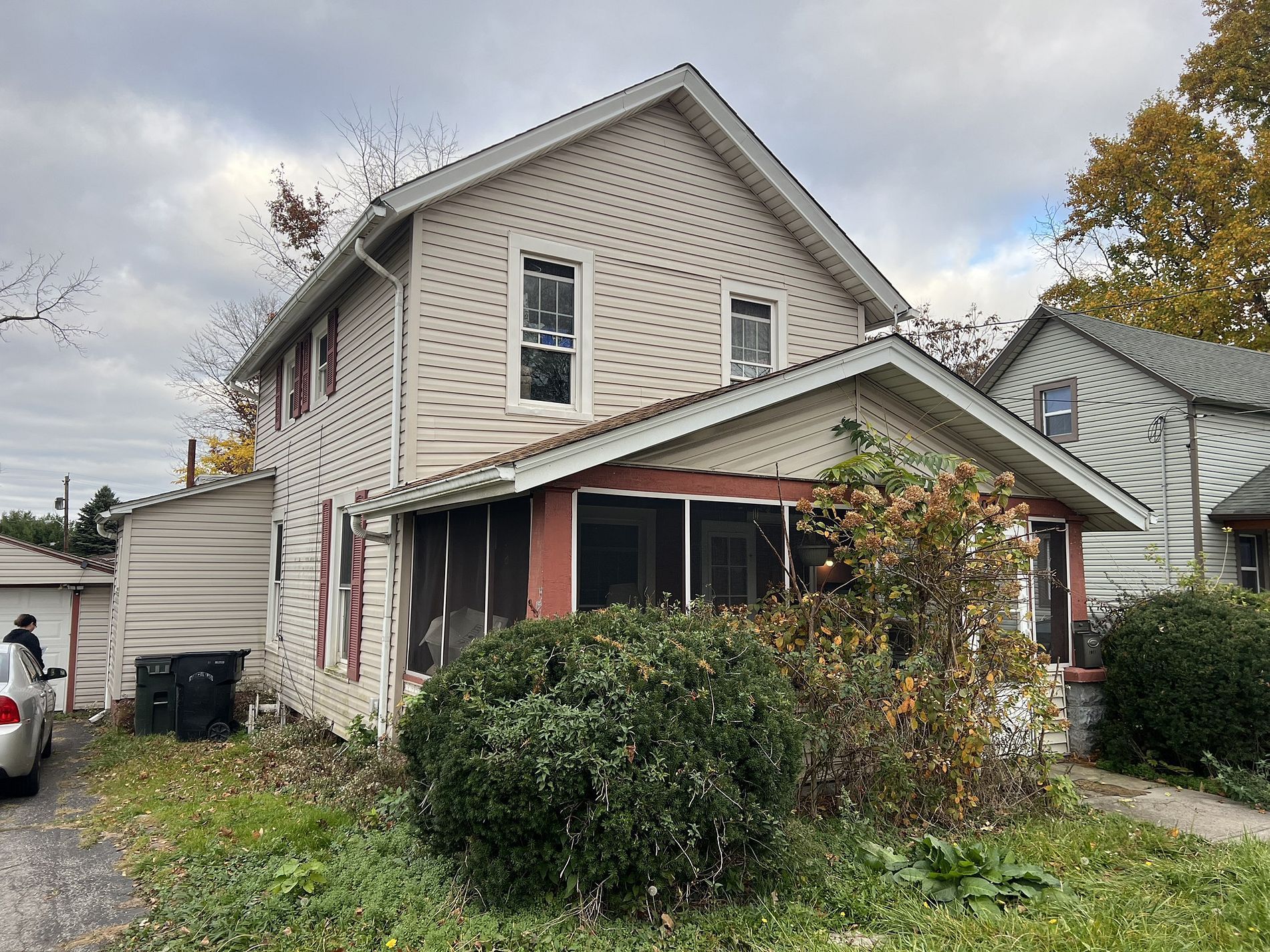 Two-story house with overgrown front yard, a screened-in porch, and detached garage.